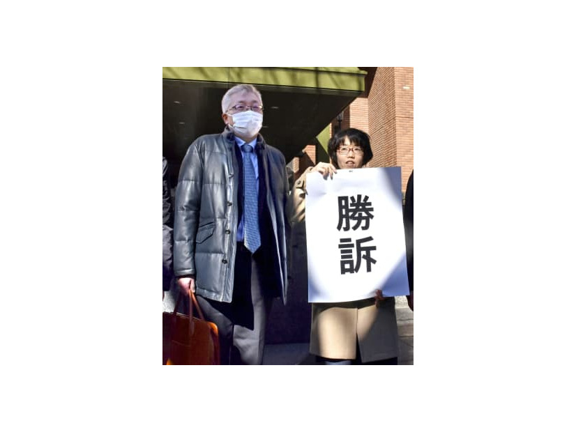 「勝訴」と書かれた紙を掲げる弁護士と原告の奥田恭正さん＝18日午後、名古屋地裁前